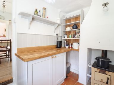 A kitchen corner with wooden countertop white cabinets kettle and shelves with teapots and jars at Warren Cottage in Bures near Assington