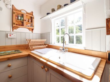 A kitchen corner with a sink under a window and wooden countertops at Warren Cottage in Bures near Assington