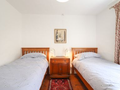 A bedroom with two single beds a wooden nightstand with two lamps and a painting on the wall at Warren Cottage in Bures near Assington