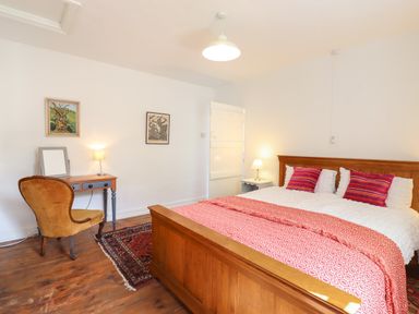 A bedroom with a wooden bed with patterned bedspread and cushions a desk with a chair and two lamps at Warren Cottage in Bures near Assington