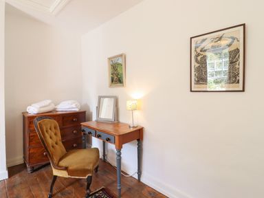 A small wooden desk with a lamp and mirror beside a vintage chair and a chest of drawers in a room at Warren Cottage Bures near Assington