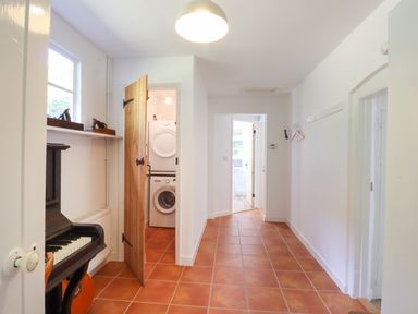 A hallway with terracotta tiled floor a piano a guitar and a laundry room with washer and dryer at Warren Cottage in Bures near Assington