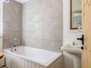 A bathroom with a bathtub a sink with a mirror and a wooden door at Warren Cottage in Bures near Assington