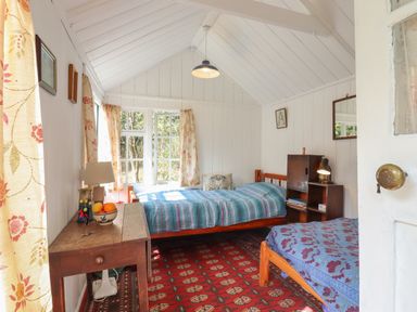 A bedroom with two single beds a wooden table with a lamp and fruit bowl and floral curtains at Warren Cottage in Bures near Assington
