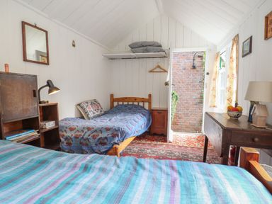 A bedroom with two single beds a wooden cabinet a desk and an open door showing a brick wall at Warren Cottage in Bures near Assington
