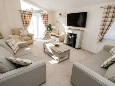 A living room with two grey sofas a beige armchair a coffee table a TV mounted above a fireplace and windows with plaid curtains at Rockpool Retreat in Runswick Bay near Hinderwell