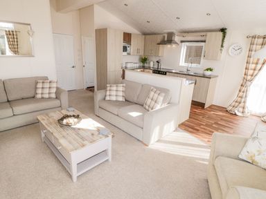 A living room with beige sofas and a wooden coffee table next to a kitchen with wooden cabinets at Rockpool Retreat in Runswick Bay near Hinderwell