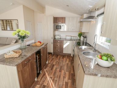 A kitchen with wooden cabinets a double sink a microwave toaster and flowers on the counter at Rockpool Retreat in Runswick Bay near Hinderwell