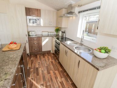 A kitchen with wooden cabinets a microwave toaster and fruit bowl on the counter at Rockpool Retreat in Runswick Bay near Hinderwell