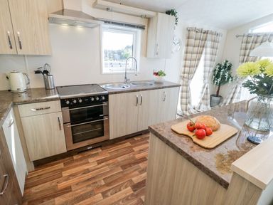 A kitchen with wooden cabinets an oven a double sink and a countertop with tomatoes and bread at Rockpool Retreat in Runswick Bay near Hinderwell