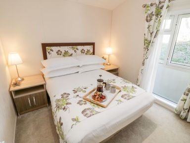 A bedroom with a double bed flanked by two bedside tables with lamps and a window with floral curtains at Rockpool Retreat in Runswick Bay near Hinderwell