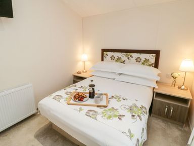 A bedroom with a double bed two bedside tables with lamps and a tray with coffee and croissants on the bed at Rockpool Retreat in Runswick Bay near Hinderwell