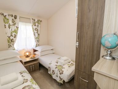 A small bedroom with two single beds a bedside cabinet with a lamp and orange juice a wardrobe and a globe on a wooden shelf at Rockpool Retreat in Runswick Bay near Hinderwell