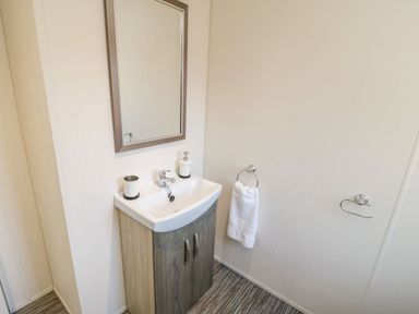 A bathroom sink with a mirror above towel ring with towel and a soap dispenser at Rockpool Retreat in Runswick Bay near Hinderwell
