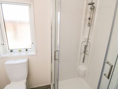 A bathroom with a toilet next to a window and a glass shower enclosure at Rockpool Retreat Runswick Bay near Hinderwell