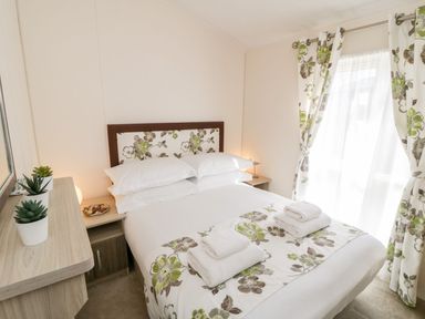 A bedroom with a bed with floral bedding and two folded towels with curtains and bedside tables at Rockpool Retreat in Runswick Bay near Hinderwell