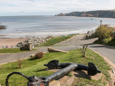 A large black anchor on grass near a curving road overlooking a beach with benches and a flagpole at Rockpool Retreat in Runswick Bay near Hinderwell