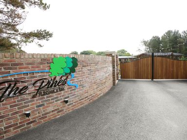 A brick wall with a sign saying The Pines at Runswick Bay and closed wooden gates at the end of a paved driveway