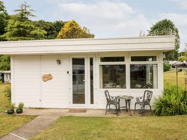 A small white house with a glass door two black metal chairs and a table outside at Ty Haf in Roch