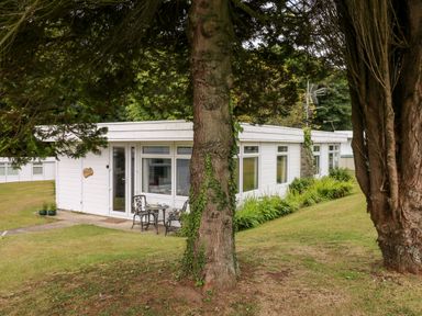 White single-story building with glass doors and windows and outdoor table and chairs on grass at Ty Haf in Roch