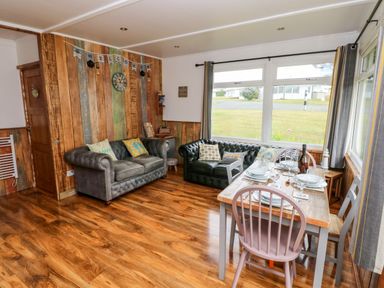 A living room with two sofas a wooden dining table and large windows at Ty Haf in Roch