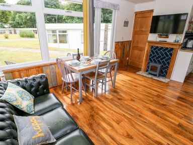 A dining area with a wooden table set for four and a black leather sofa next to large windows and a fireplace at Ty Haf in Roch