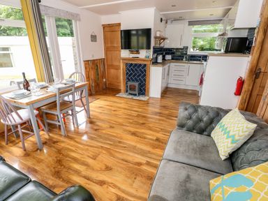 A living area with a dining table set by windows a kitchen with white cabinets and a wood floor at Ty Haf in Roch