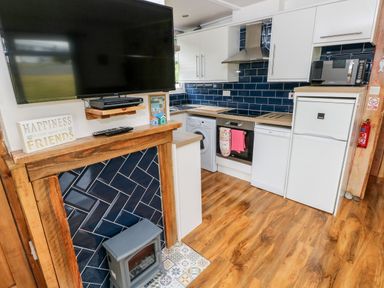 A kitchen with white cabinets blue tile backsplash washing machine oven and a fireplace with a mounted television at Ty Haf in Roch