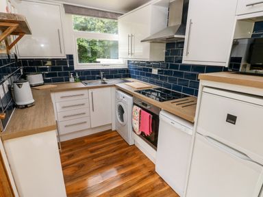 A kitchen with white cabinets blue tile backsplash wooden countertops and wooden floor at Ty Haf in Roch