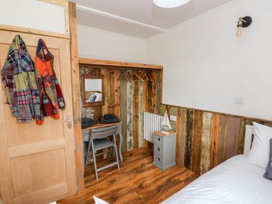 A bedroom corner with a wooden desk and chair a mirror coats hanging on a wooden door and a small cabinet with a model sailboat at Ty Haf in Roch