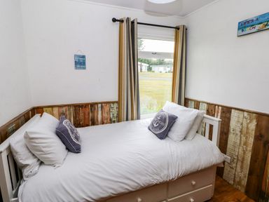 A bedroom with a single bed and striped curtains on the window at Ty Haf in Roch