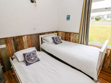 A bedroom with two single beds with white bedding and decorative pillows next to a window at Ty Haf in Roch