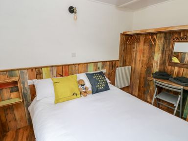 A bedroom with a bed with pillows and a teddy bear a wooden wall with hangers a small desk and chair at Ty Haf in Roch