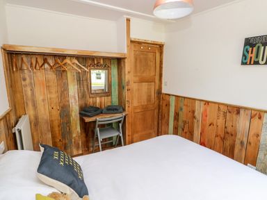A bedroom with a bed cushions hangers on a wooden wall and a small desk at Ty Haf in Roch