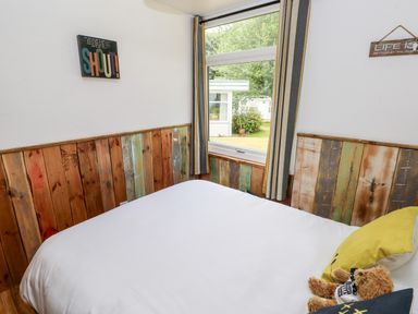 A bedroom with a bed white bedding wooden panel walls and a window showing outside at Ty Haf in Roch