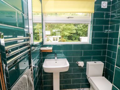 A bathroom with a white sink and toilet green tiled walls and a window with a yellow blind at Ty Haf in Roch