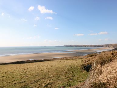 A coastline with a sandy beach and grassy land under a blue sky at Ty Haf in Roch