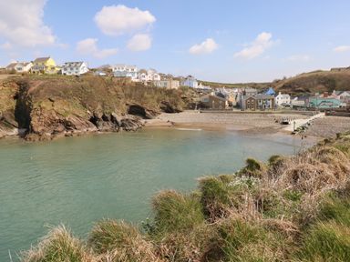 A coastal village with houses on a cliff and a small beach with water at Ty Haf in Roch