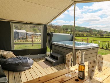 A covered outdoor decking area with a hot tub bean bag seating and a wooden table with glasses and a bottle at The Salmon in Nantmel near Rhayader