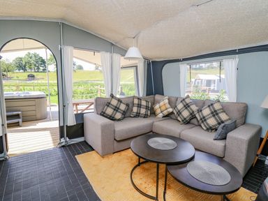 An enclosed seating area with a corner sofa and two round tables overlooking a deck with a hot tub at The Salmon in Nantmel near Rhayader