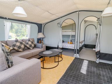 A seating area with a sofa with plaid cushions a floor lamp and two round tables in a tent with bunk beds visible through doorways at The Salmon in Nantmel near Rhayader