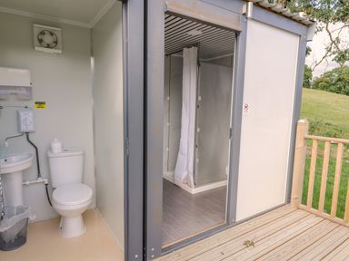 A compact bathroom with a toilet sink and shower visible through an open door on a wooden deck at The Salmon in Nantmel near Rhayader