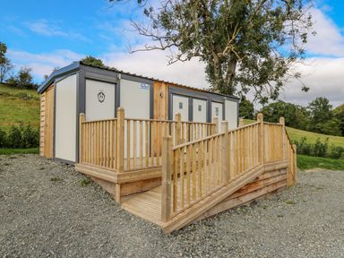 A wooden ramp leading to outdoor restroom units in a grassy area at The Salmon in Nantmel near Rhayader