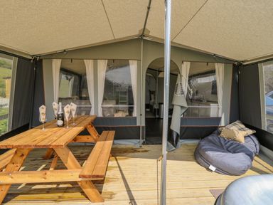 A covered outdoor seating area with a wooden picnic table and benches a bean bag with cushions and a bottle with glasses at The Salmon Nantmel near Rhayader