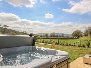 An outdoor hot tub with bubbling water overlooking a fenced grassy field with hills and trees at The Salmon Nantmel near Rhayader