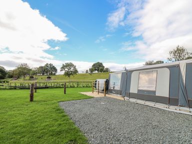 A caravan with gravel and grass in a field with trees and a blue sky at The Salmon in Nantmel near Rhayader