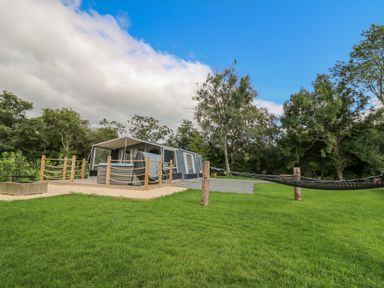A grassy outdoor area with a tent and hammock surrounded by trees at The Salmon in Nantmel near Rhayader