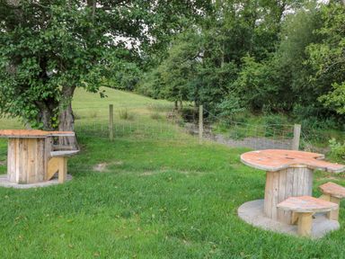 A grassy outdoor area with two wooden spool tables and benches near trees and a wire fence at The Salmon in Nantmel near Rhayader