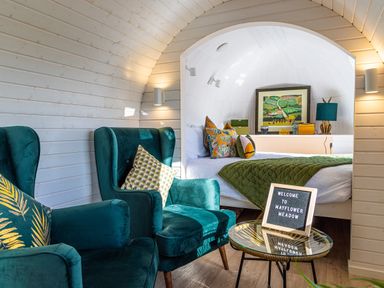 A room with two teal armchairs a small round glass table with a welcome sign and a bed with green quilt and colorful pillows at Veiko - Mayflower Meadow in Burshill near Brandesburton