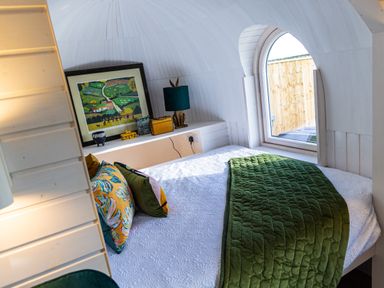 A bedroom with a bed with a green blanket and pillows next to an arched window at Veiko - Mayflower Meadow in Burshill near Brandesburton
